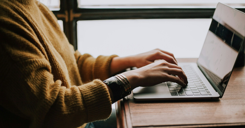 A close-up from the side of a woman sitting at a table using a laptop