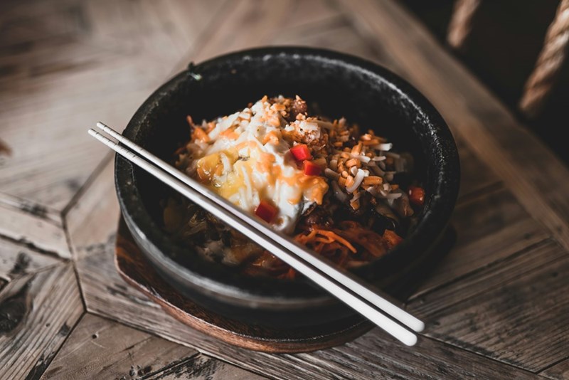 A bowl of rice with veggies and two chopsticks on top.