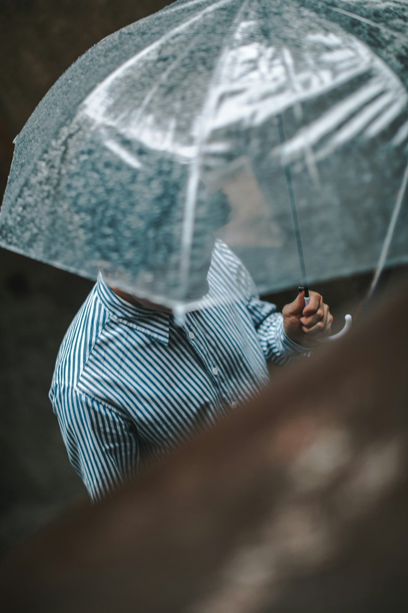 A well-dressed man in a button-up shirt holds a clear umbrella in the rain (stock).