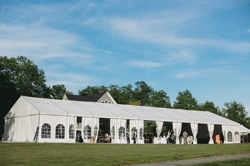 A large wedding tent catering to an event with hundreds of guests outdoors. (stock)