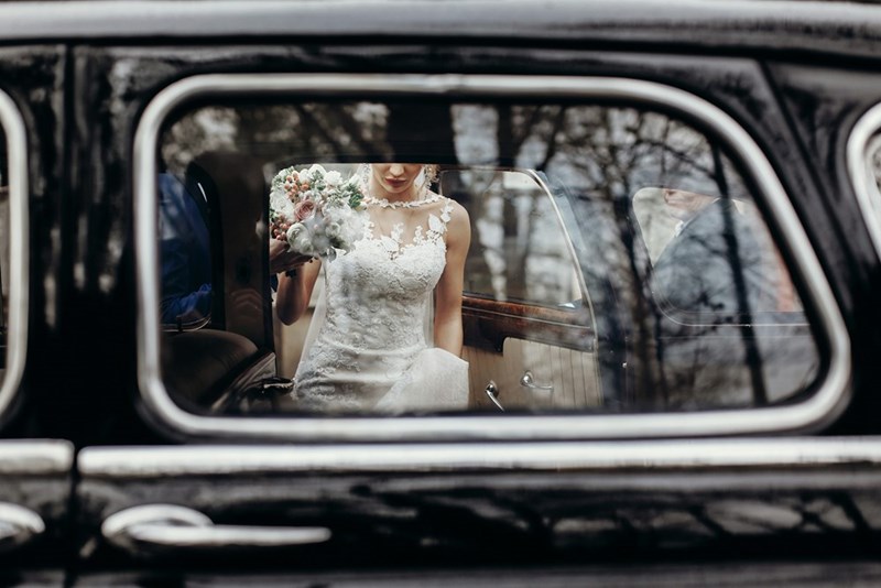 A bride gets escorted to a nice car while her guests are sent to a catered bus. (stock)