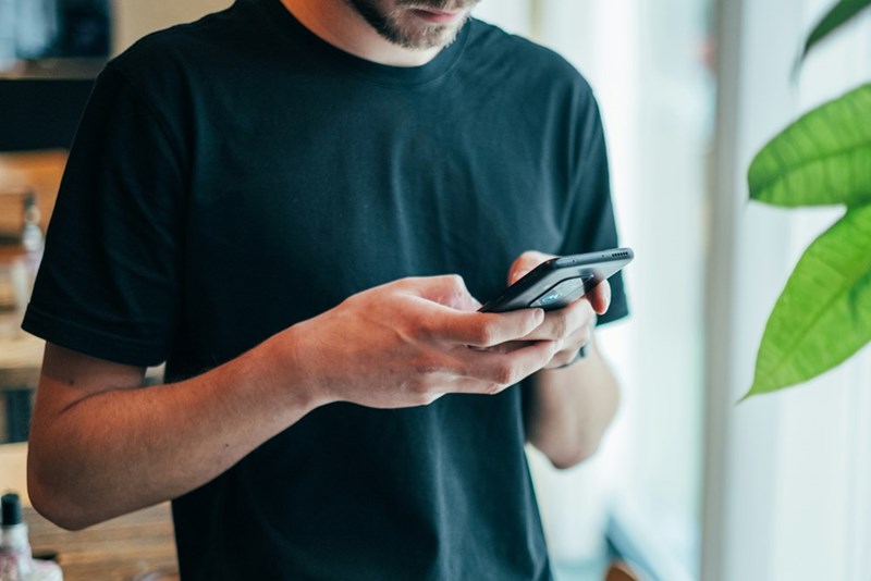 Men with beard and a black shirt sending a message with his cell phone.