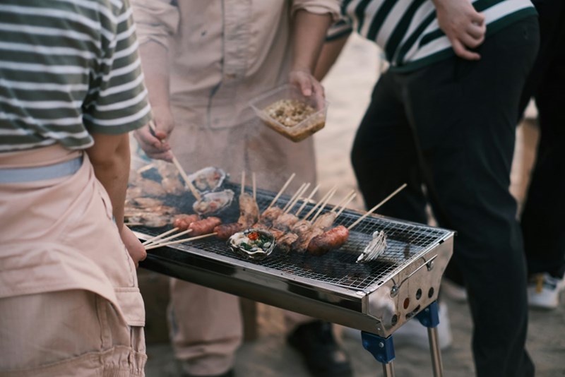 a group of people standing around a grill with food on it