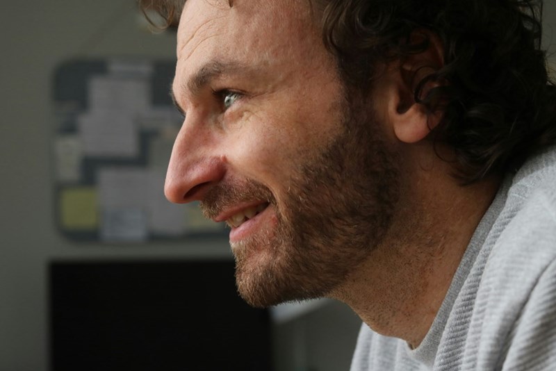 Close-up of a man smiling in profile indoors with a softly blurred background.