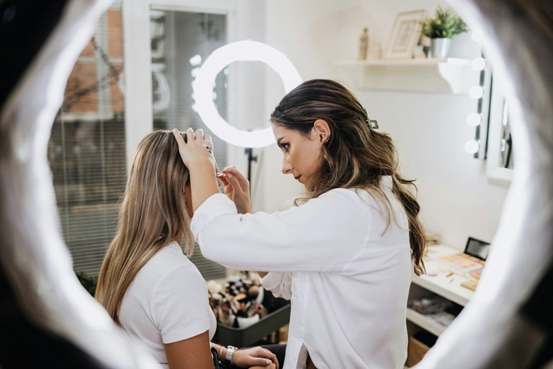A woman in white professionally applies makeup to another woman for a film set.