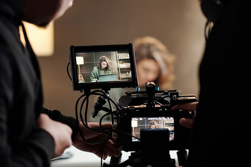 The view from a professional camera's viewing screen, recording an actress at a table.