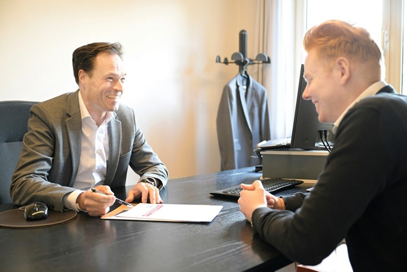 two smiling men discussing documents at an office desk