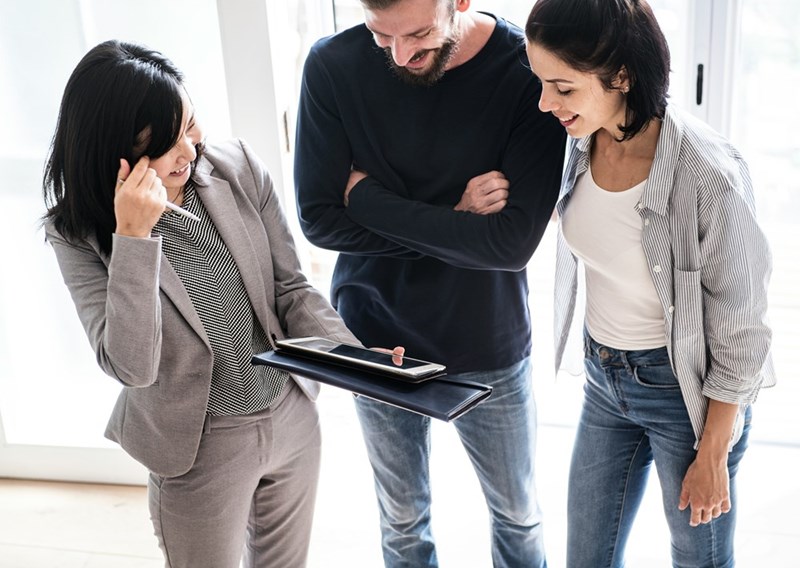 Real estate agent showing property details to a couple, with both leaning in and smiling as they review information together, as shown by models.