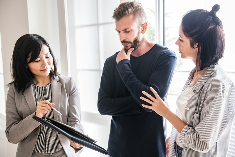 Couple listening carefully to a real estate agent, with thoughtful expressions suggesting they are weighing an important housing decision, as shown by models.