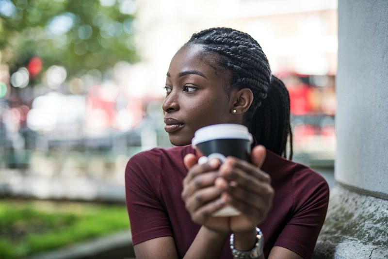 A model representing a woman holding a coffee cup while staring thoughtfully to the side, appearing deep in reflection about a personal or financial dilemma.
