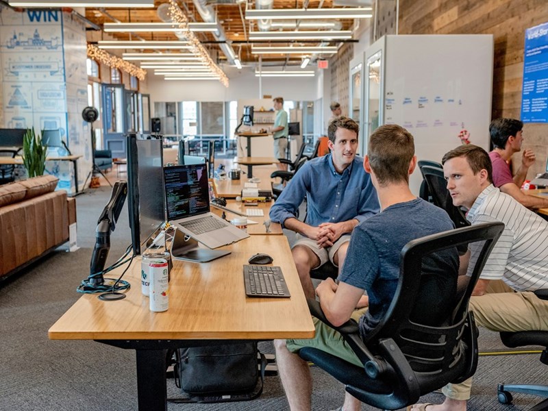 Three men talking to each other while at work in an office.