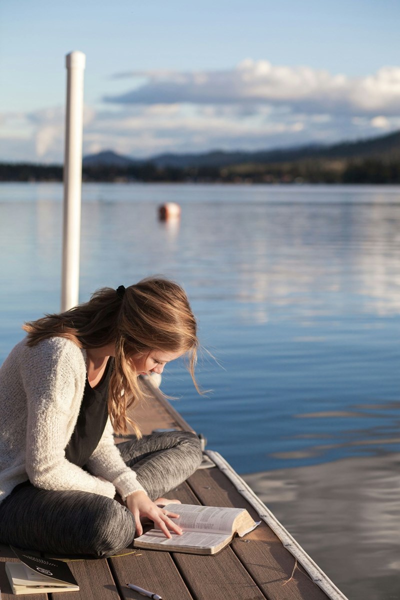 woman reading book near body of water