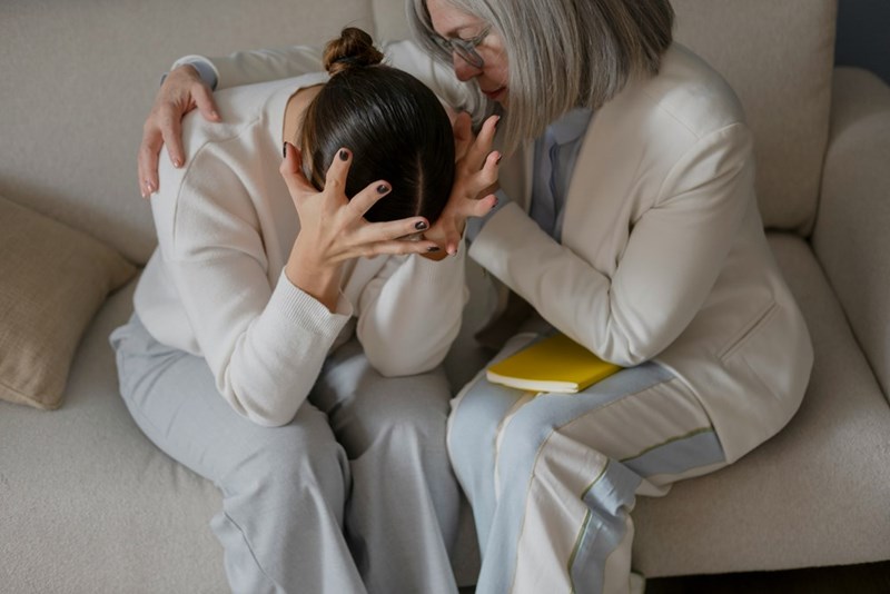 Mother and adult daughter hugging in the couch.