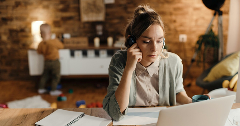An employee works from home and takes a call, with a baby playing in the background