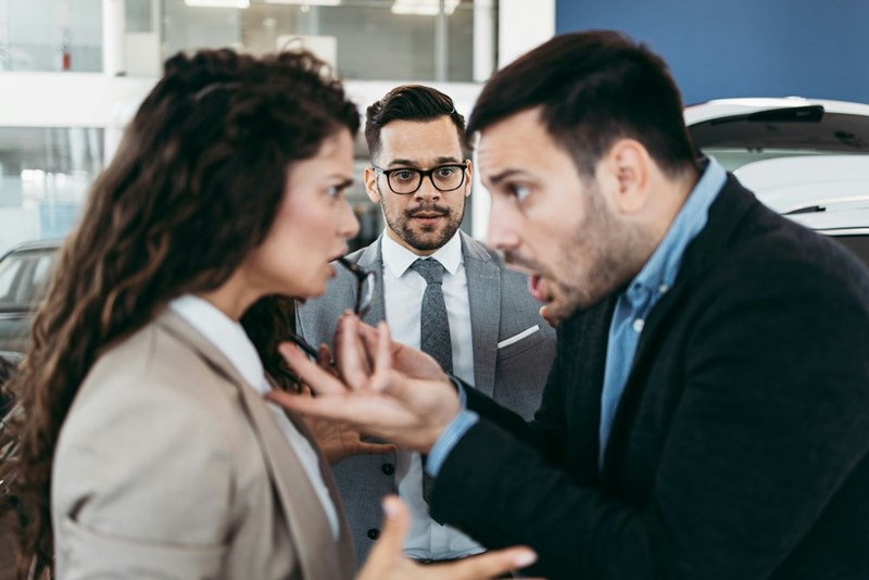 A pair of people argue in the foreground while a colleague stands in the background