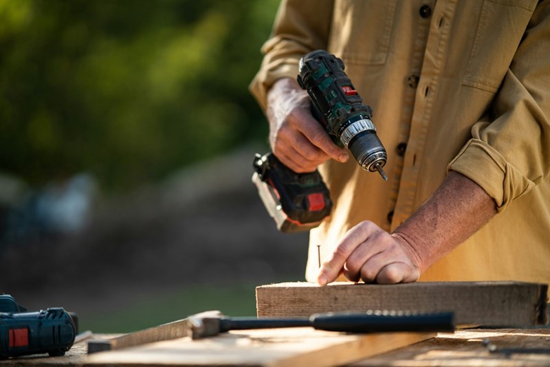 Property owner using power tools and lumber materials while building or repairing a fence on residential land.