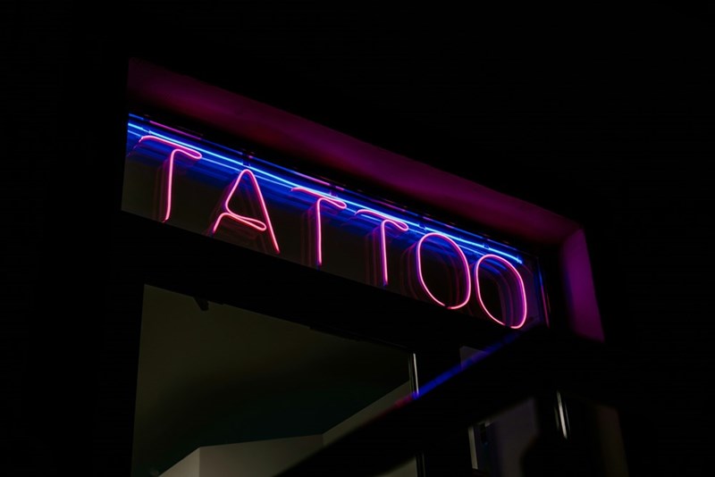 A neon sign of a tattoo shop where an unsatisfied client returned to get her tattoo redone.