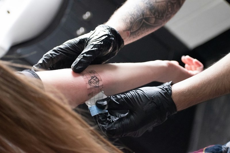 A tattoo artist applying a stencil to a client’s forearm, illustrating the approval step before permanent ink is added.