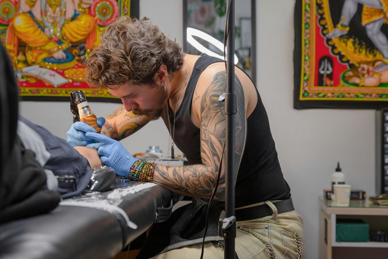 A tattoo artist in blue gloves tattooing a client's skin, illustrating why fresh ink cannot simply be redone immediately.