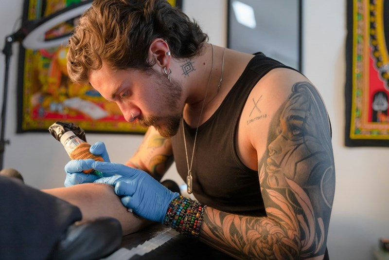 A close-up of a tattoo artist working on script-style ink, showing the permanent nature of a design approved by the customer.