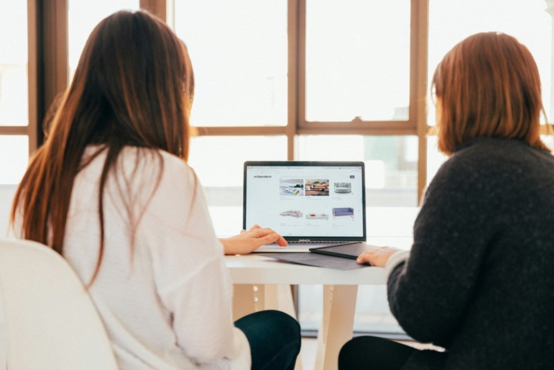 Two women are talking while they look at the screen of a computer.