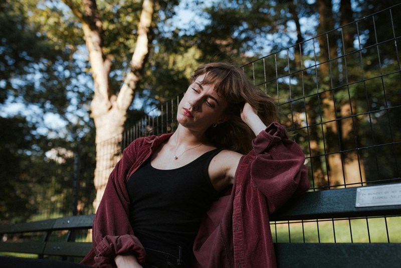 Young woman leaning back on a park bench with a distant, hurt expression.