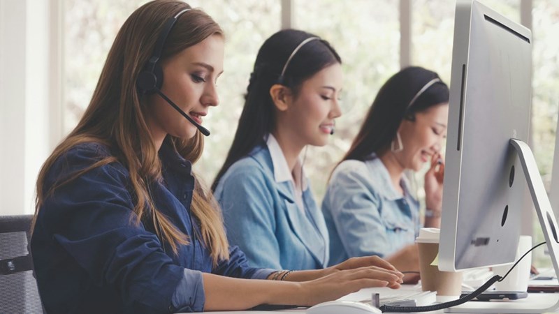 Customer support representatives wearing headsets while assisting clients and managing service requests at their workstations.