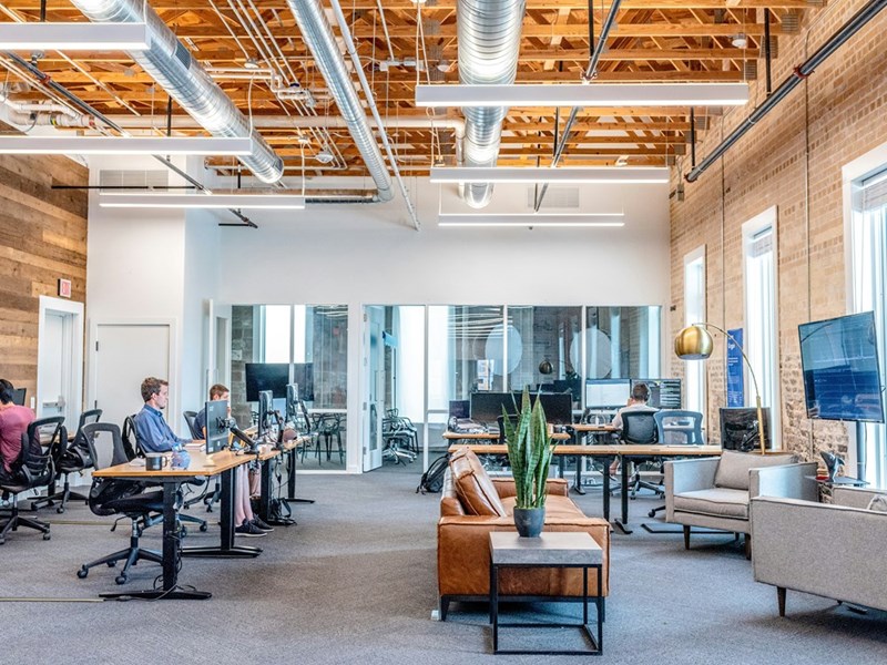Open-plan office with employees working at computer stations, desks, and collaborative workspaces during a regular business day.