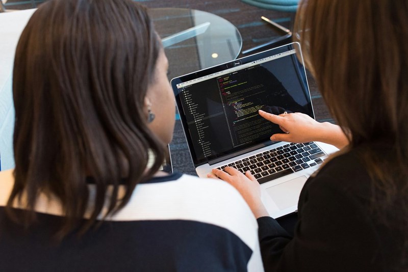 IT professionals reviewing software code on a laptop during a workplace collaboration session involving technical support, systems management, and software development.