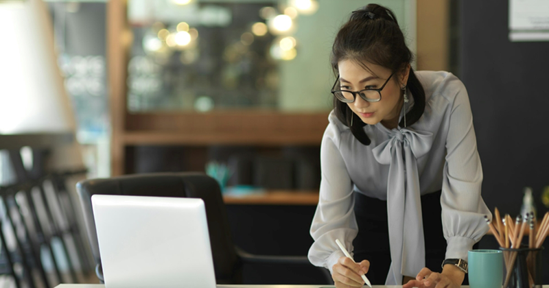 A female employee leans over a desk to look at a laptop