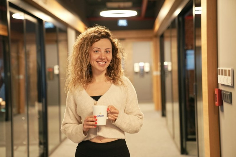 A co-worker looks at you in the office hallway while holding a coffee, ready to chat your ear off.