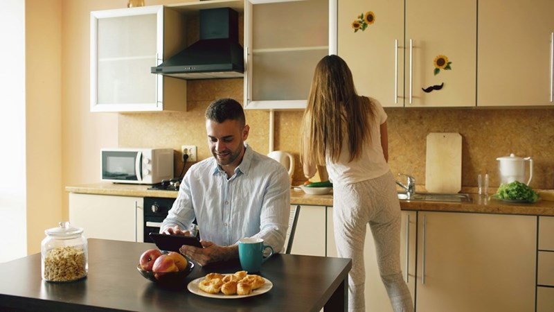 Couple in the kitche, man using tablet woman preparing food.