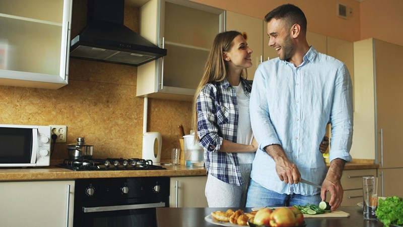 Couple in kitchen smiling and cooking.