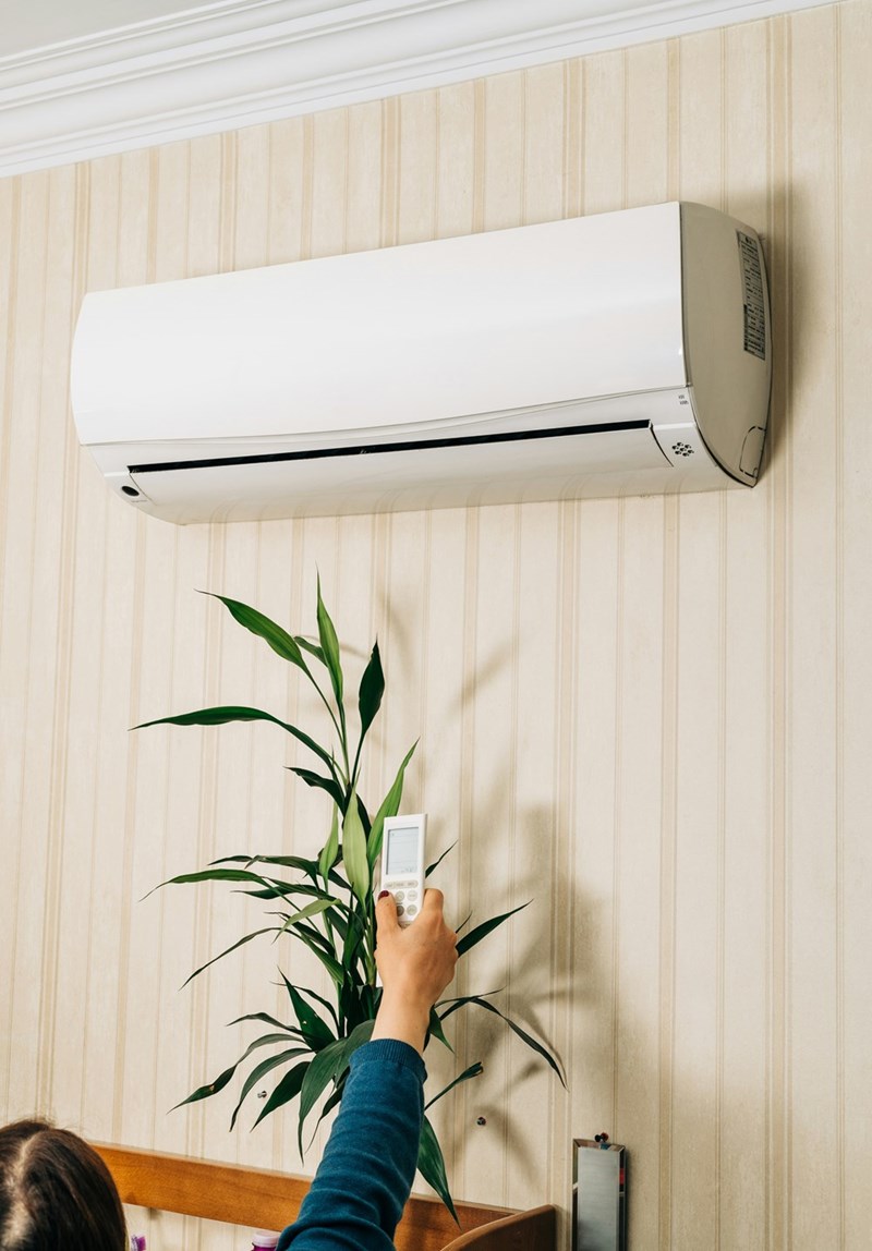 Residential air conditioning unit mounted on an interior wall as a homeowner adjusts the remote control.