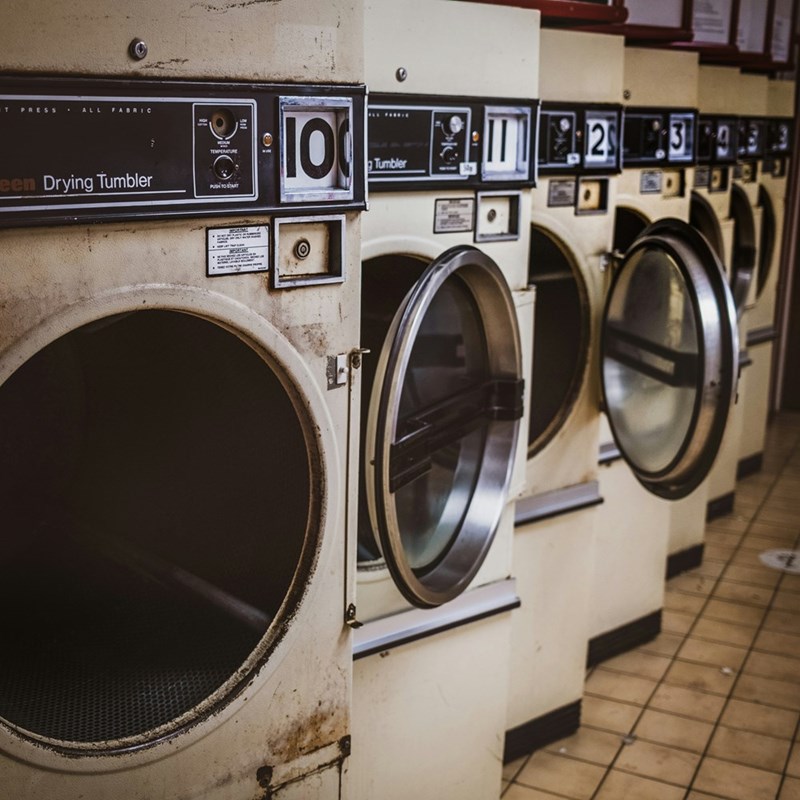 Row of old commercial dryers in a laundromat with open machine doors.