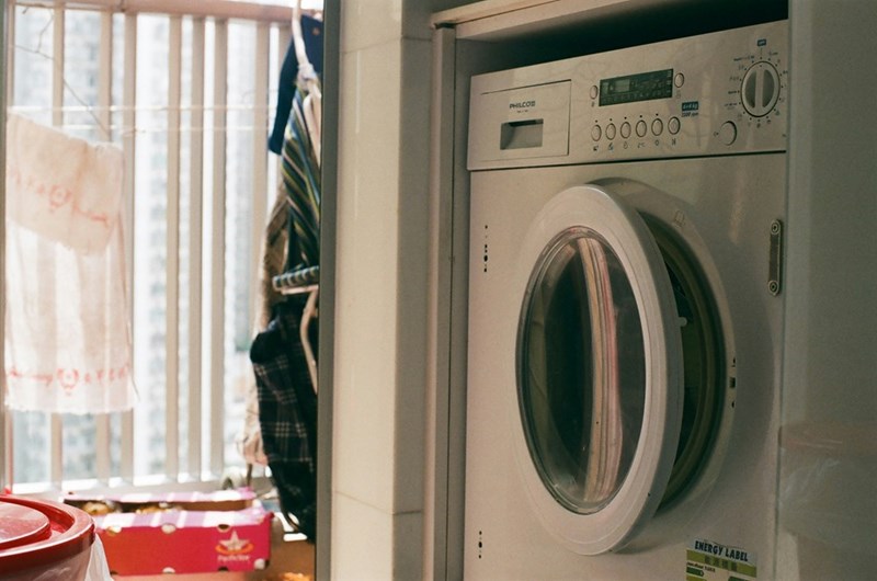 Front-loading washing machine installed inside a residential laundry area near a window with hanging clothes.