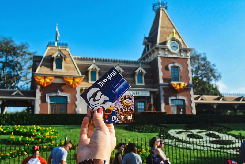 A Disney fanatic holds a ticket to Disneyland in front of the entrance to the park. She doesn't care where she got it from, because she's going to enjoy her day at Disney no matter what. 