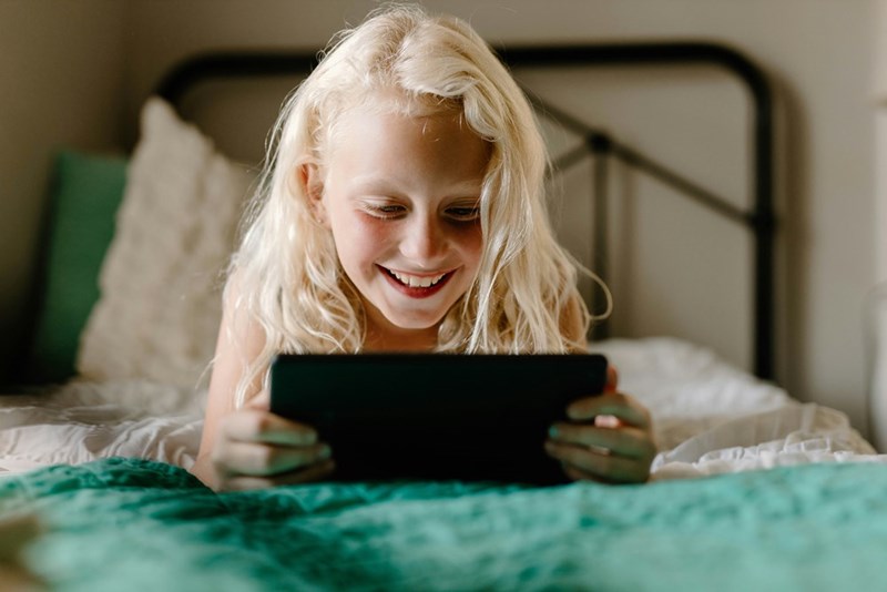 A young child using a tablet at home, representing the 7-year-old half-sister whose parents want to give her an older laptop.