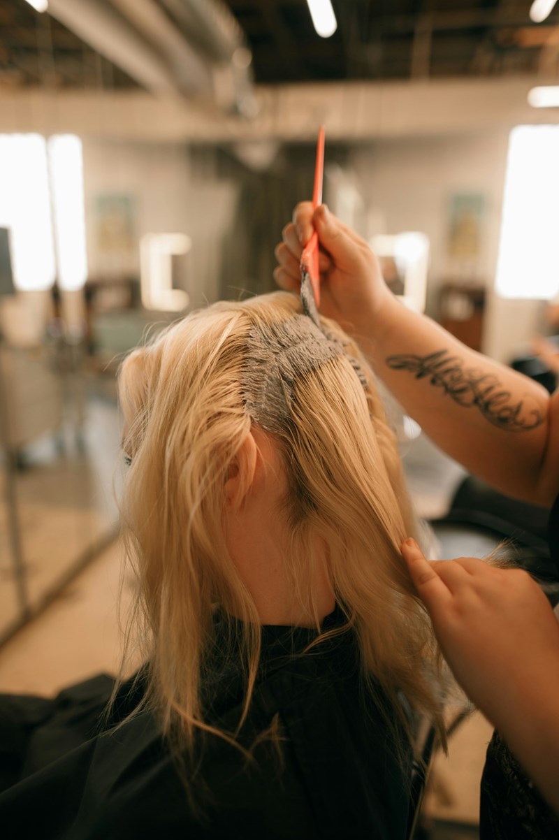 A hair stylist fixes the roots of one of his blonde clients whose roots have grown in a couple of inches. 