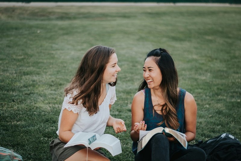 two woman laughing sitting on the grass