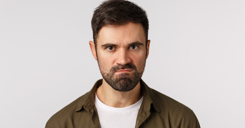 Man frowning straight at the camera in an olive overshirt against a plain light background.