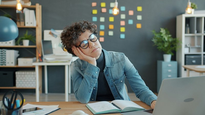 Remote employee sitting at a desk and looking away from a laptop while thinking through a task.