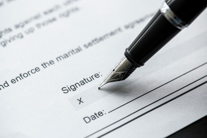 Close-up of a legal document signature line with a fountain pen positioned above the signing area.
