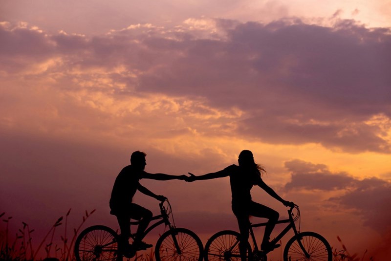 Visual representation of a woman on a bicycle holding the hand of a man behind her, also on a bike.