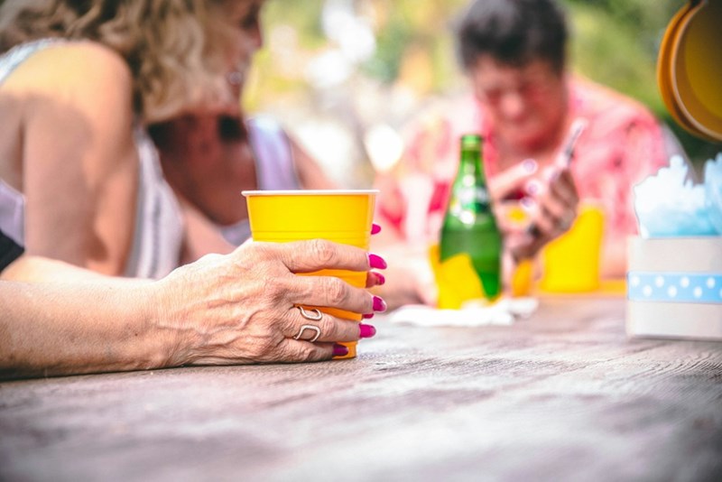 Older woman holds a plastic yellow cup at an outdoor birthday party.