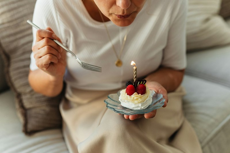 Older woman enjoys a birthday cupcake with a birthday candle burning, as she prepares to blow it out and make a wish.