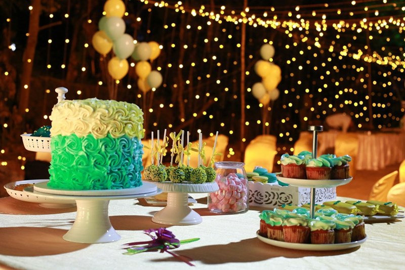 Model image of a cake, cupcakes, and other baked goods displayed on a table surrounded by birthday decorations.