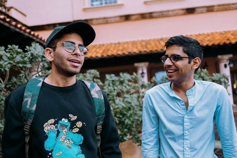 Two adult brothers talking outdoors in a residential courtyard.