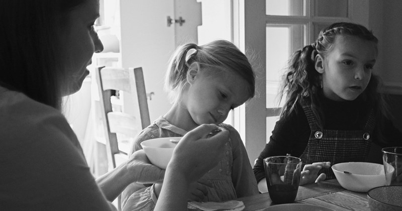 Two young girls and their mom eat breakfast together at a kitchen table