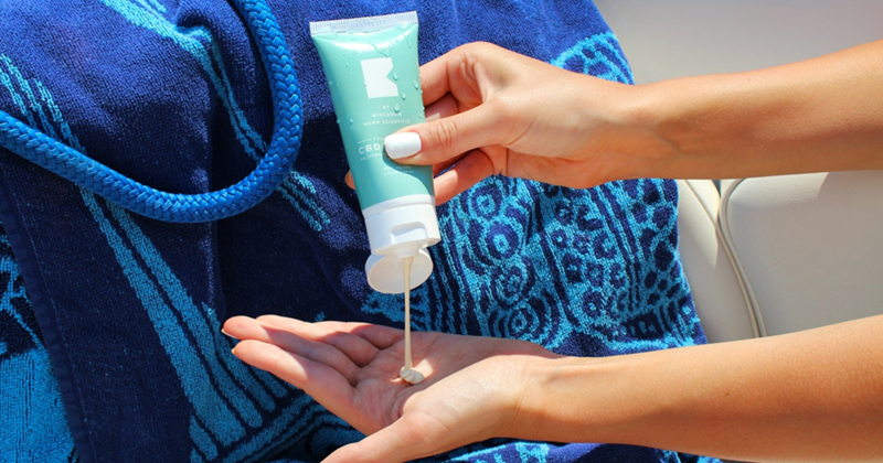 A representation of a close-up of a woman squeezing sunscreen into her hand in front of a towel